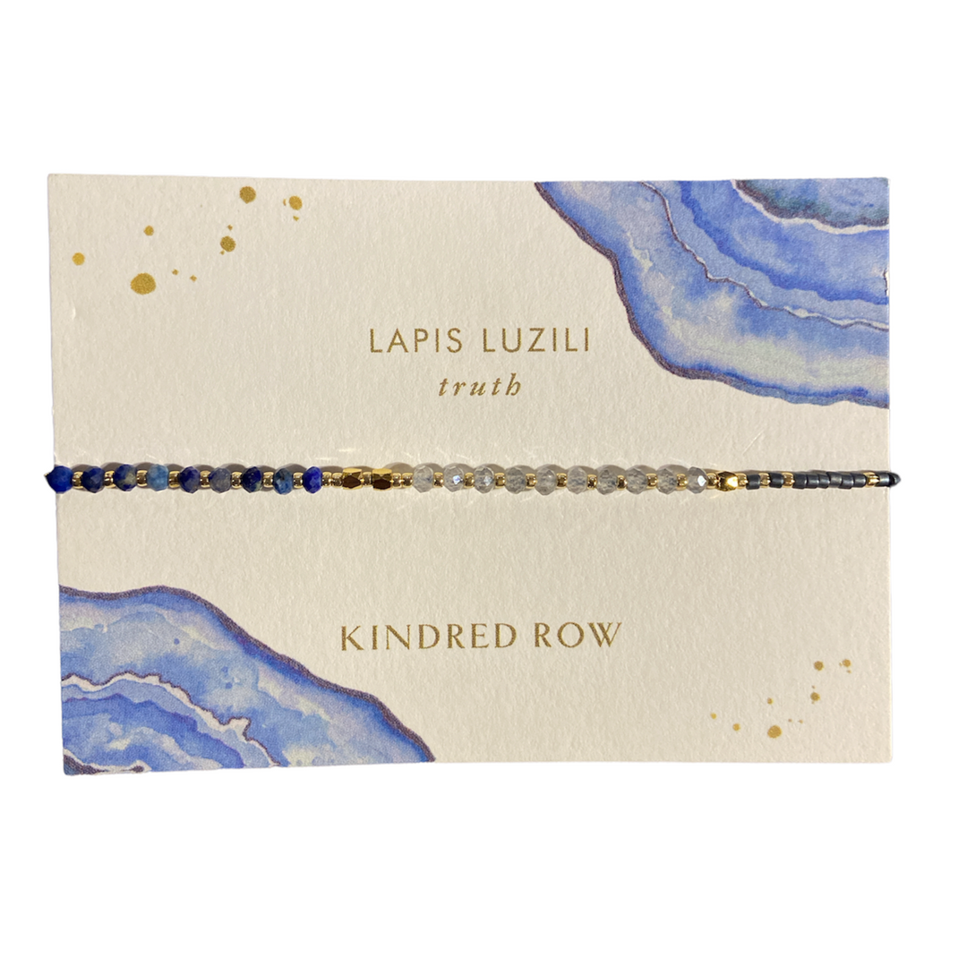 Displaying the Lapis Lazuli Healing Gemstone Stacking Bracelet by Kindred Row, this delicate handmade bracelet showcases a pattern of blue, clear, and gold beads along with natural gemstones and an adjustable cord. Presented on a card adorned with watercolor designs, it features the inscriptions "Lapis Lazuli truth" and "Kindred Row.