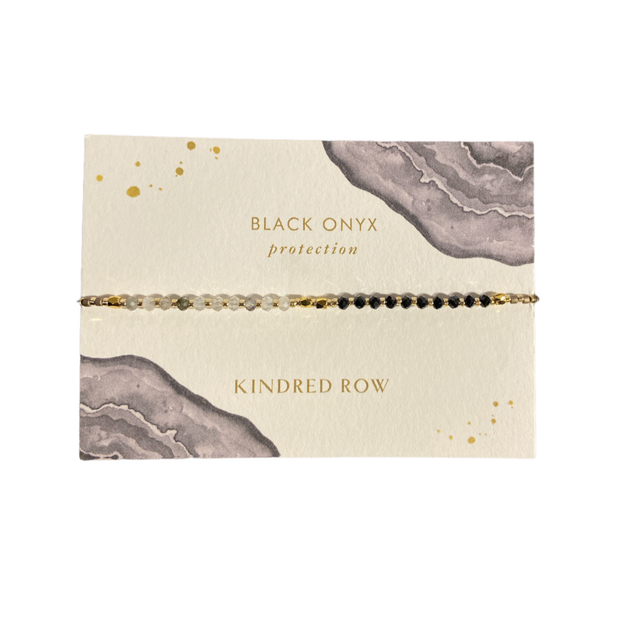 Presented on a decorative card, the Black Onyx Healing Gemstone Stacking Bracelet from Kindred Row is a piece of handmade jewelry that highlights gray and gold abstract patterns. It features the text "Black Onyx Protection" and is crafted with natural gemstones, showcasing alternating black and clear beads on an adjustable cotton cord.