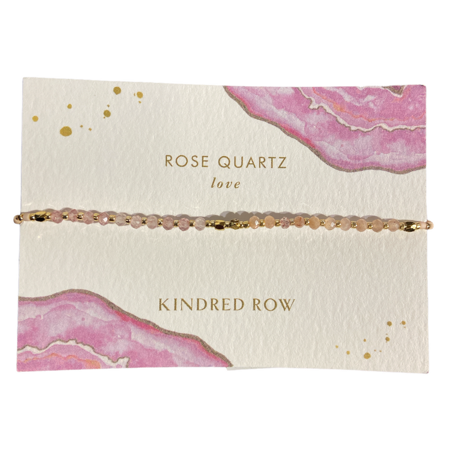 A Rose Quartz Healing Gemstone Stacking Bracelet, crafted from natural gemstones, showcases small beads on a decorative card adorned with pink and gold abstract designs. The card features the text: "ROSE QUARTZ love" and "KINDRED ROW.