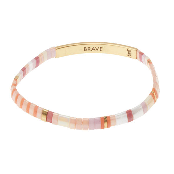 The Scout Jewelry Miyuki Brave Gold bracelet features pink, peach, and white Japanese glass beads with a 14K gold-dipped bar inscribed "BRAVE" and alternating gold beads.