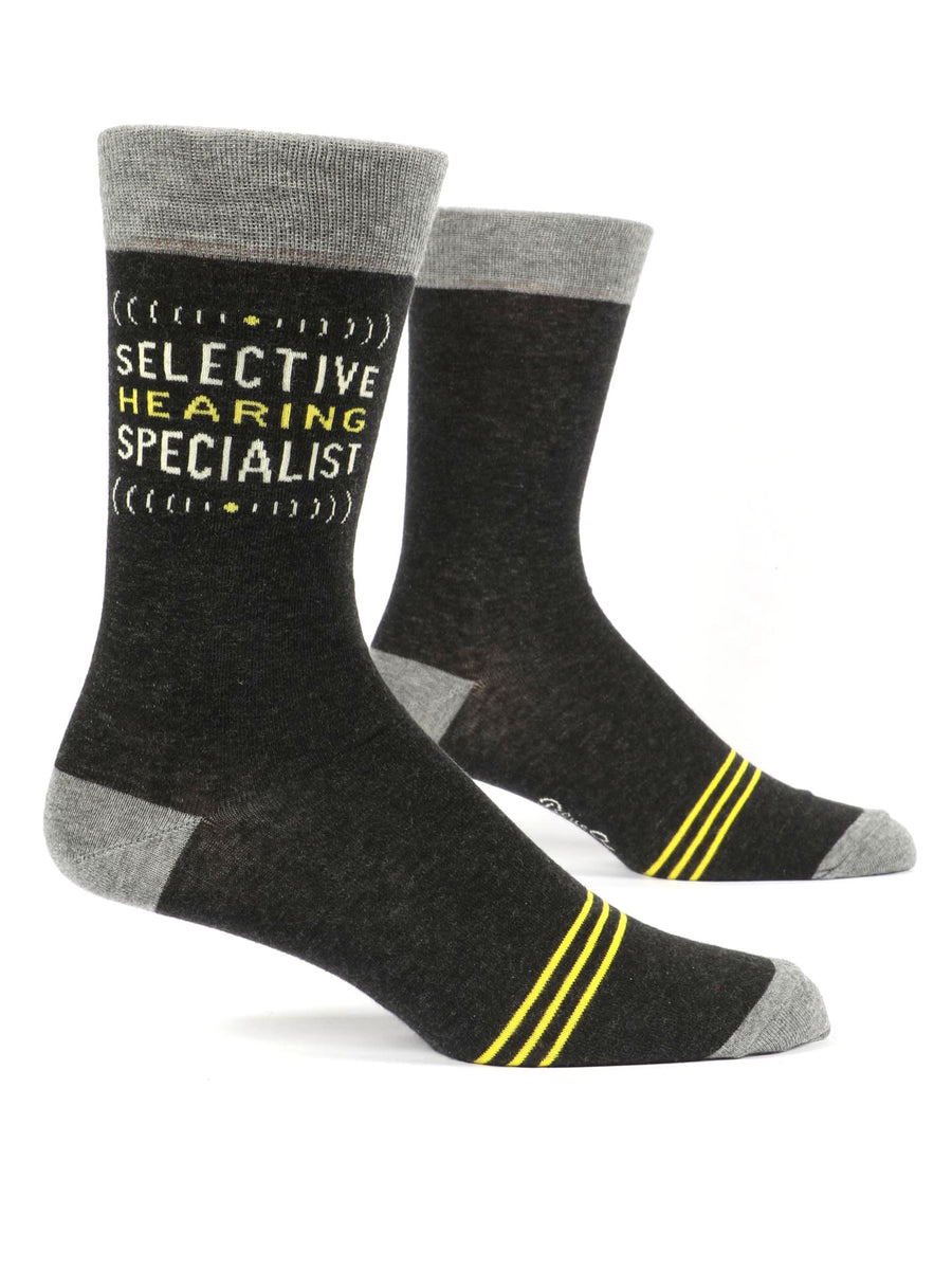 Blue Q's Selective Hearing Socks are made from combed cotton and feature a pair of black socks with gray cuffs, heels, and toes. Both socks include two yellow stripes near the toes, and one sock is emblazoned with the phrase "SELECTIVE HEARING SPECIALIST" in yellow text. These men's socks are displayed standing upright on an invisible display.