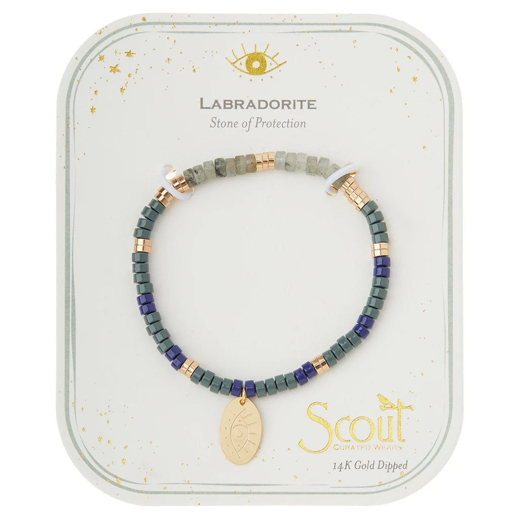 Displayed on a light background is Scout Jewelry's "Intention Charm Labra/Gold" beaded bracelet, crafted from labradorite stones with gold-colored accents. The bracelet features a small 14K gold-dipped charm adorned with an eye symbol. Text above reads "Labradorite Stone of Protection," and below, "Scout, semi-precious stones.