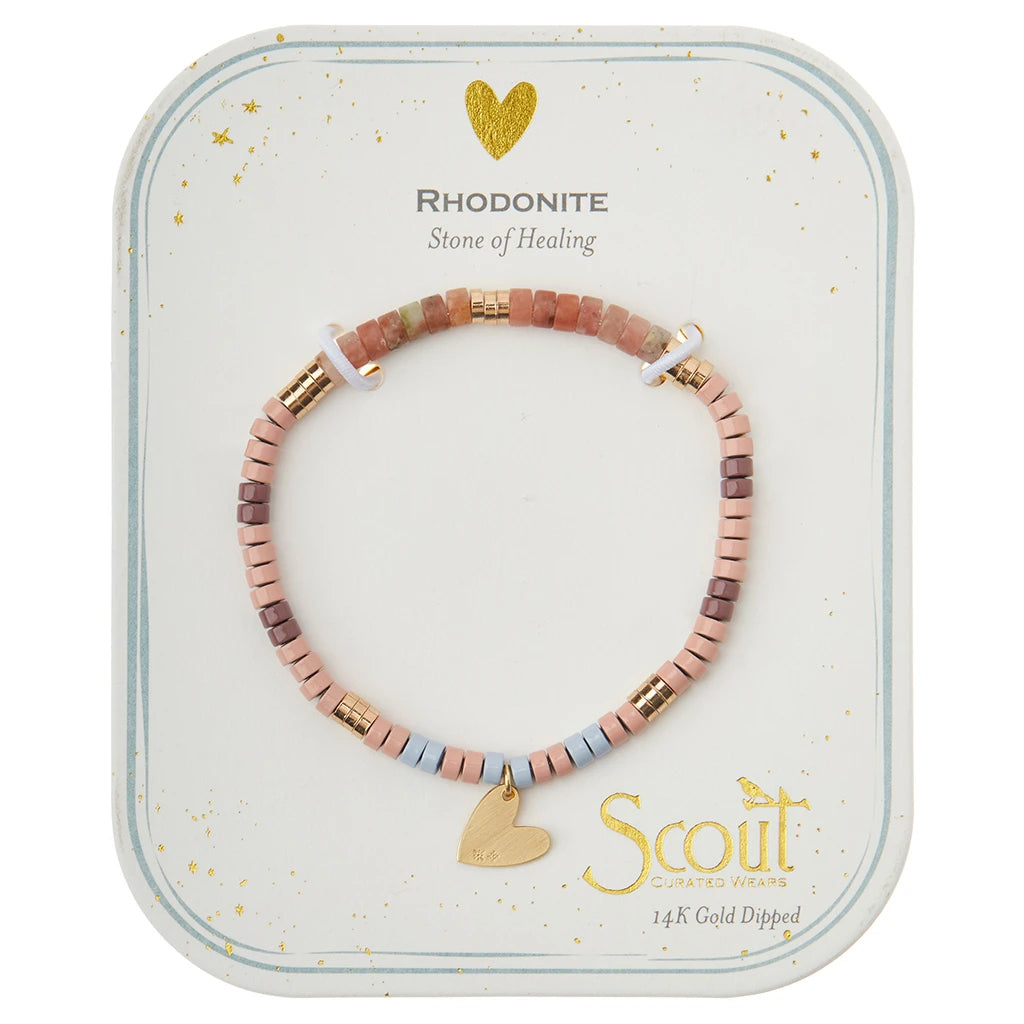 The Intention Charm Rhod/Gold by Scout Jewelry features a bracelet crafted with pink, blue, and purple square beads accented by occasional gold beads and a small gold heart charm. It is elegantly displayed on a white card with gold detailing, bearing the phrases "Rhodonite Stone of Healing" and "Scout Curated Wears 14K Gold Dipped." This piece exudes positive intention.