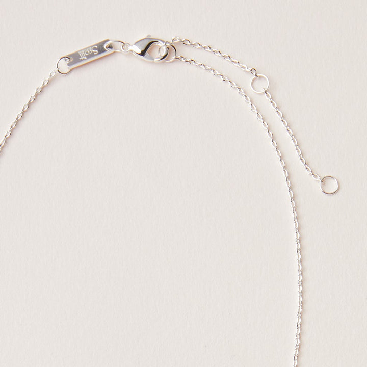 Close-up of the Intention Neck Tourmaline/Silver by Scout Jewelry, a delicate silver necklace with an adjustable chain and clasp featuring a small engraved tag. Displayed on a light-colored surface, its elegance is highlighted.