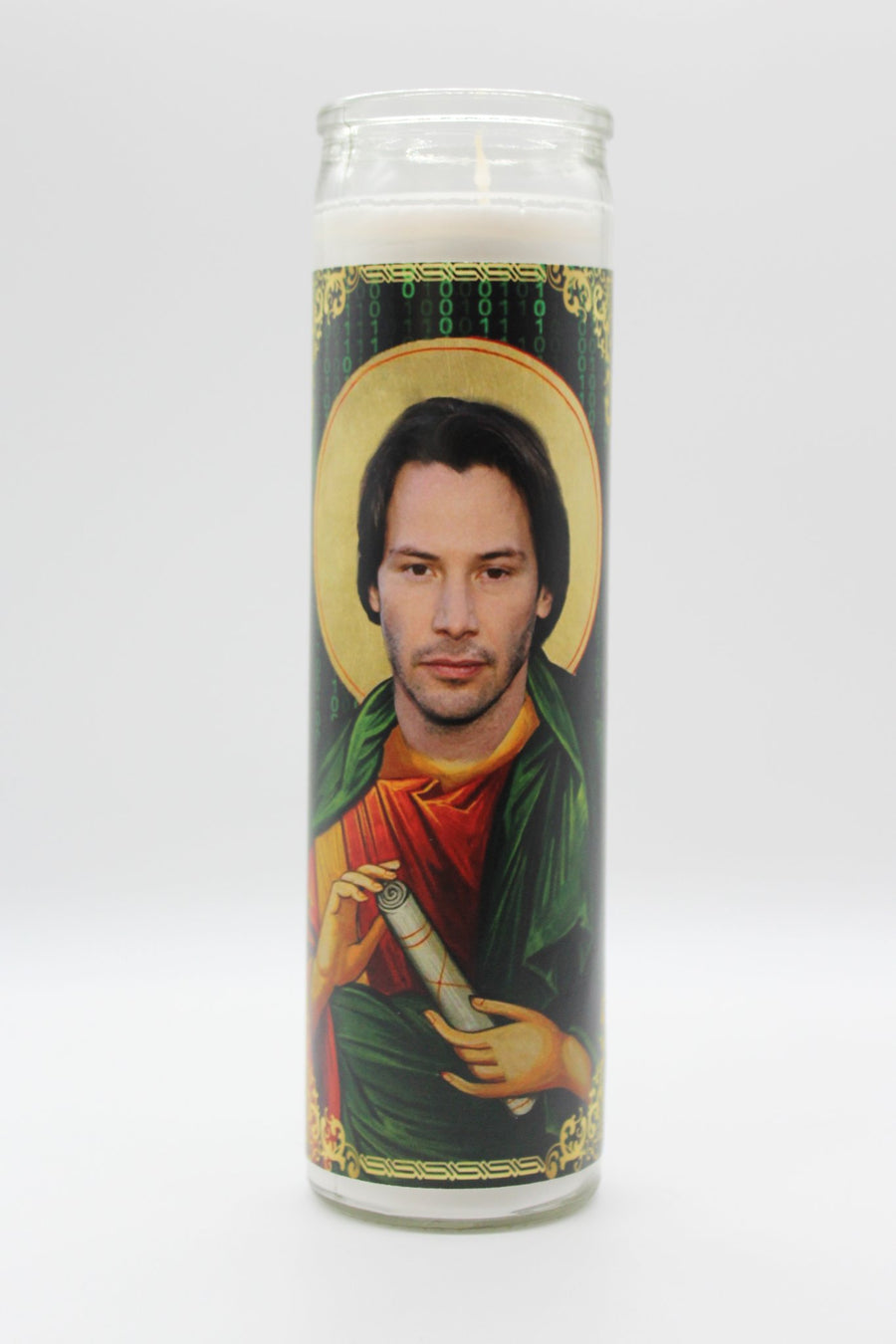 The Keanu Reeves Candle by BOBBYK BOUTIQUE is a tall glass candle with an image of a saint-like figure with long hair holding a scroll, against a mystical, green pattern reminiscent of digital code.