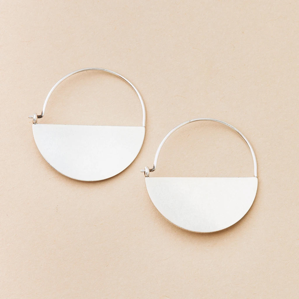 A pair of Lunar Hoop Silver earrings by Scout Jewelry is displayed on a beige background. Each hypoallergenic earring features a semi-circular, smooth sterling silver piece hanging from the bottom half of a thin, circular hoop.