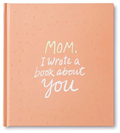 The hardcover book "Mom I Wrote a Book About You" by Compendium has a peach-colored cover adorned with light polka dots. The title is displayed in a combination of yellow and white handwritten fonts. Filled with meaningful prompts, it serves as the ideal heartfelt gift to capture shared experiences.