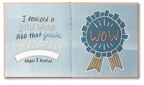 An open book titled "Mom I wrote a book about you" by Compendium reveals an illustrated page declaring, "I realized a little while ago that you're even more than I knew." On the opposite page, there's a blue ribbon with the word "WOW" in the center. This heartfelt gift beautifully encapsulates shared experiences.