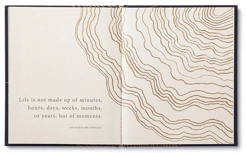 A cherished family keepsake, "Most of All" by Compendium, opens to reveal an abstract pattern of gold lines on cream and offers timeless wisdom. The left page features the quote: "Life is not made up of minutes, hours, days, weeks, months, or years, but of moments.