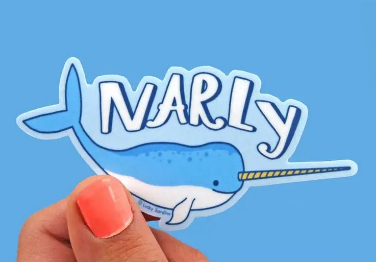 A hand with coral-colored nail polish holds the adorable, scratch-resistant Narly Narwhal Sticker from Lucky Sardine, showcasing a cheerful blue narwhal. The word "NARLY" is written in large, playful letters above the narwhal on a weatherproof blue background.