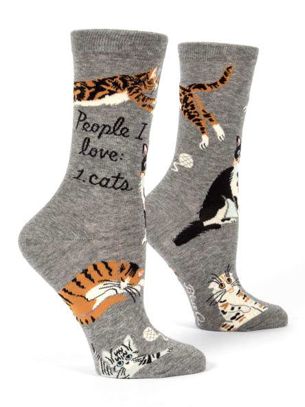 The Blue Q People I Love: Cats Crew Socks feature various cat illustrations in playful and relaxed poses on a gray background. With text on one sock that reads "People I love: 1. cats," these socks are made from soft combed cotton and fit women's shoe sizes 5-10. The vibrant colors and detailed patterns stand out, making these socks a purr-fect choice.