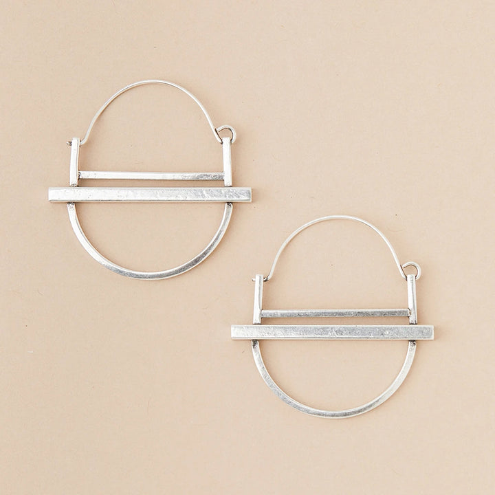 The Saturn Hoop Silver earrings by Scout Jewelry are showcased on a beige background. Each hypoallergenic earring features an open circular design intersected by a horizontal bar at the bottom, with a lightweight semi-circle below it, highlighting a minimalist and modern aesthetic.