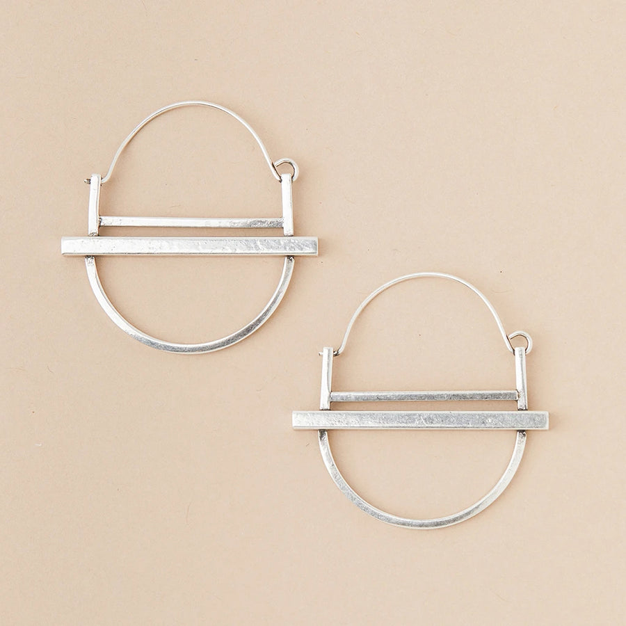 The Saturn Hoop Silver earrings by Scout Jewelry are showcased on a beige background. Each hypoallergenic earring features an open circular design intersected by a horizontal bar at the bottom, with a lightweight semi-circle below it, highlighting a minimalist and modern aesthetic.