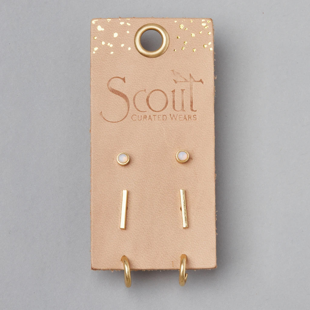 The Scarlett Stud Trio Opalite Gold from Scout Jewelry is beautifully showcased on a beige leather card with "Scout Curated Wears" embossed in gold letters. This elegant presentation includes gold-colored stud earrings and matching linear drop earrings. The card, adorned with a few decorative gold specks and featuring a small hole at the top, proudly indicates that these hypoallergenic earrings are as safe as they are stylish.