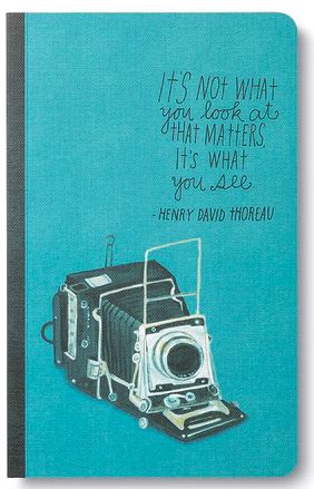 Introducing the "Its Not What You Look At" notebook from COMPENDIUM, featuring a teal cover with an illustration of a vintage camera. On the cover, elegant typography displays a quote by Henry David Thoreau: "It's not what you look at that matters, it's what you see." Inside, you'll find lined pages ideal for capturing your thoughts and inspirations.