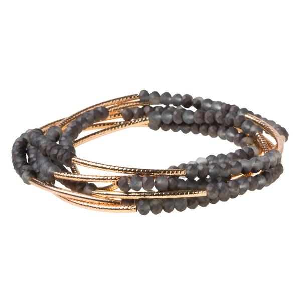 The Wrap storm/gold bracelet by Scout Jewelry showcases small dark beads intertwined with gold-colored elements, offering an elegant layered look.