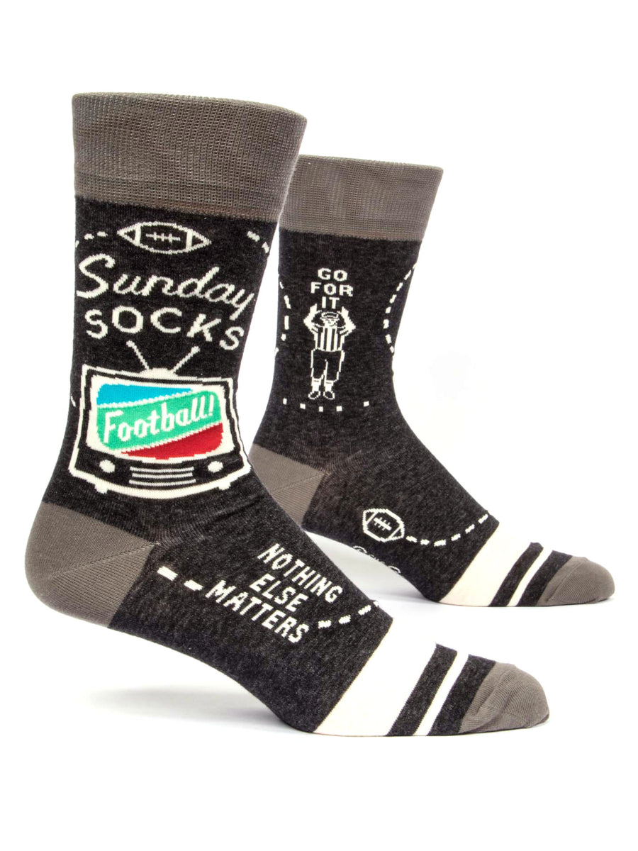 Blue Q's Sunday Socks are gray with black, white, and teal accents, showcasing football-themed designs. One sock features a TV screen with the word "Football" along with the phrases "Sunday Socks" and "Nothing Else Matters." The other sock displays an image of a referee and the words "Go for it." These socks pair perfectly with sweatpants for ultimate game-day comfort, making them an excellent gift for any football fan.