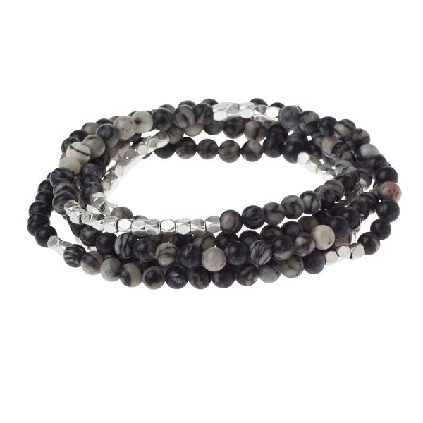 Introducing the Stone Wrap black agate/silver by Scout Jewelry: A versatile multi-layered bracelet, adorned with an elegant assortment of black and white marbled beads, interspersed with small silver accents. With its 34" length, this chic piece effortlessly transitions from a stacked bracelet to a sophisticated necklace, adding a touch of elegance to any outfit.