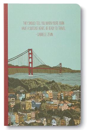 The product features an illustration of a cityscape with vibrant buildings and a red bridge over water, beautifully designed to enhance its charm. The cover displays the text, "They should tell you when you're born: have a suitcase heart, be ready to travel. - Gabrielle Zevin," in modern typography that complements the aesthetic. This item is part of the COMPENDIUM brand and titled "They should tell you when.