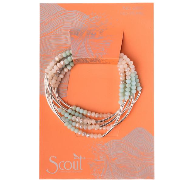 A set of beaded bracelets in turquoise and silver tones is displayed on an orange card, featuring decorative patterns and the words "No Grit No Pearl" from Scout Jewelry's Wrap collection.