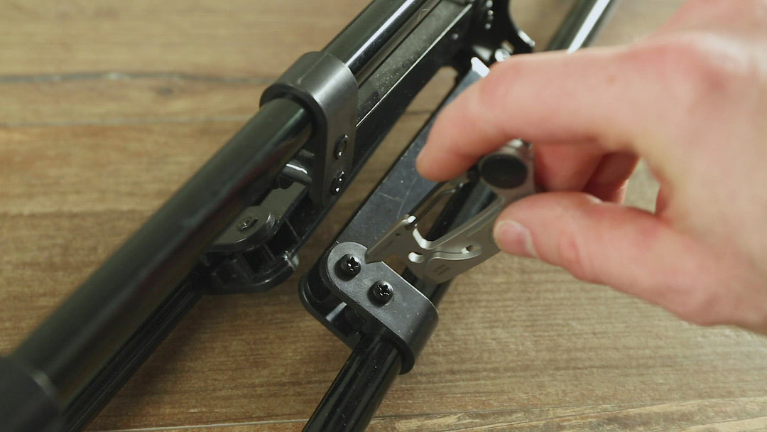 A close-up of a hand using the KeySmart Raptor Keychain Multitool to tighten or adjust a part on a black metal frame on a wooden surface. The tool, an essential multi-functional gadget, engages with a bolt or screw on the frame—a must-have for any outdoors adventurer.