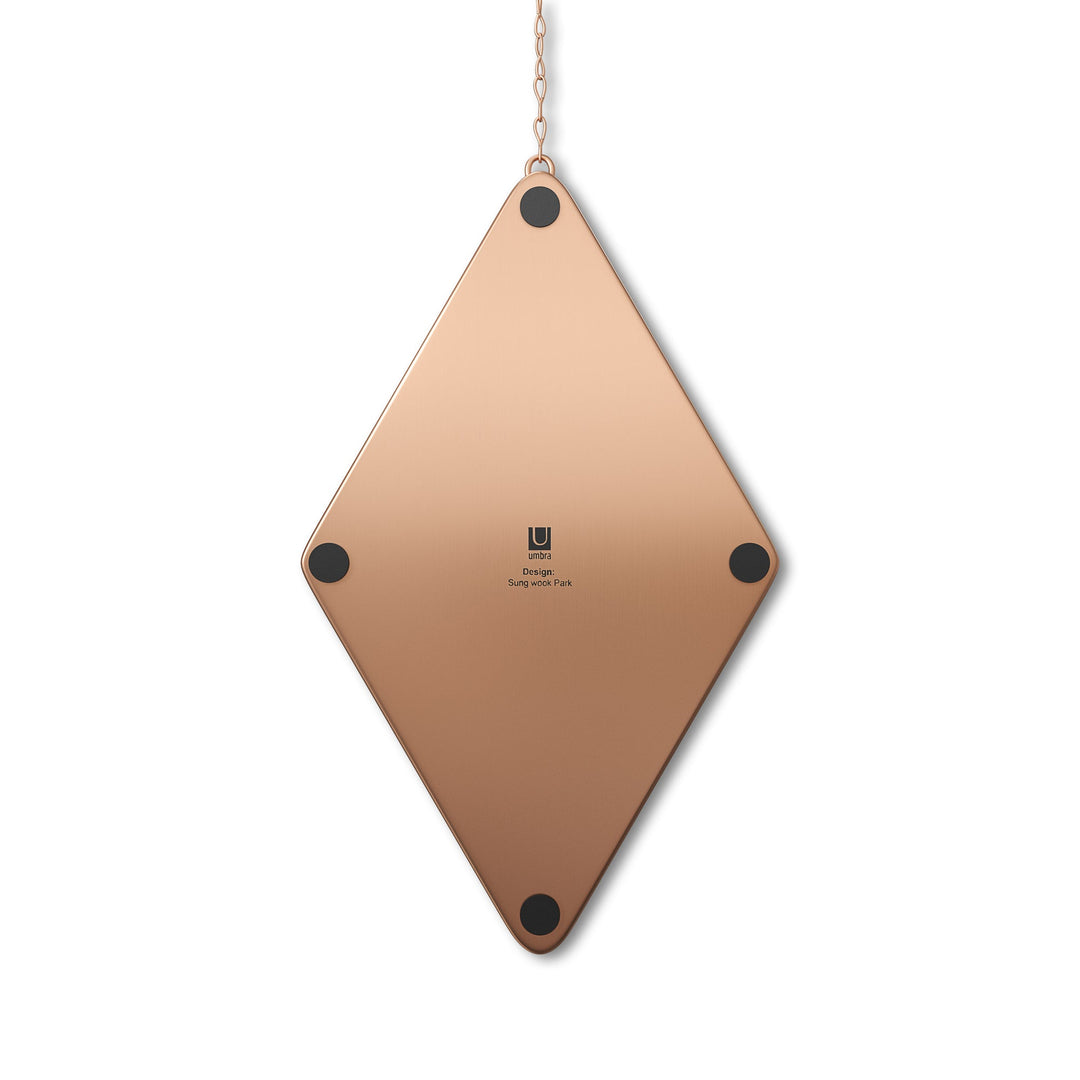 The Diamond Mirror Brass by Umbra hangs elegantly from a chain, featuring a diamond shape with four black dots at each corner and a center logo. Its bronze color is set off against a plain white background.